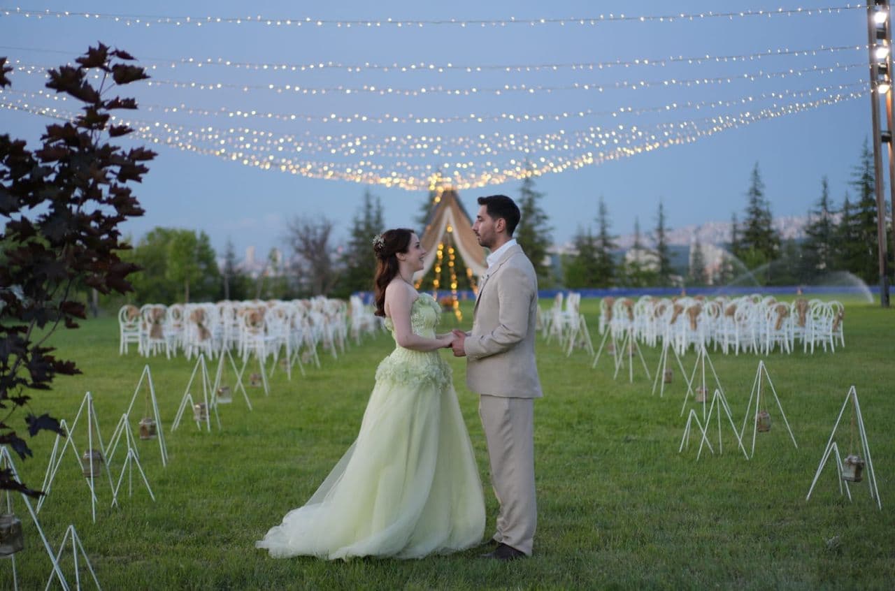 Işıklar altındaki nikah alanında el ele gülümseyen gelin ve damat