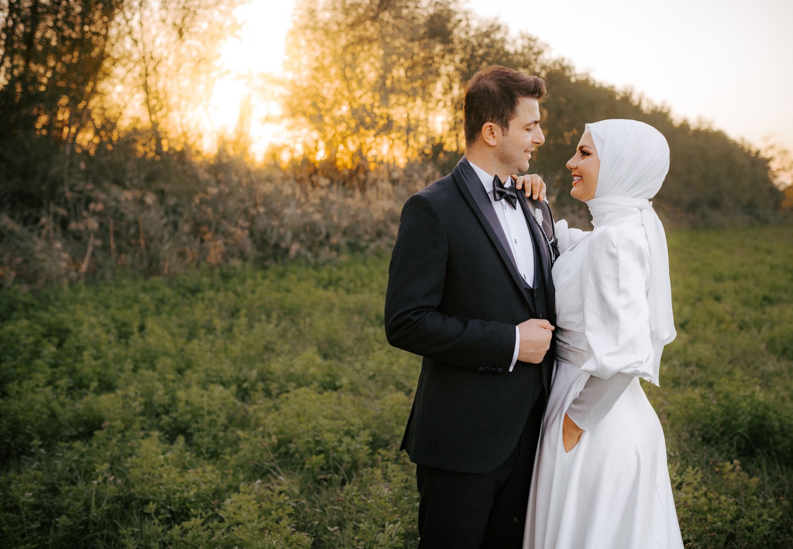 Gün batımında yeşillikler arasında tesettürlü gelin ve damat